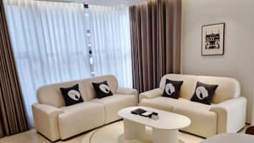 A modern living room with a beige sofa set, a round coffee table, and a large window with sheer curtains.