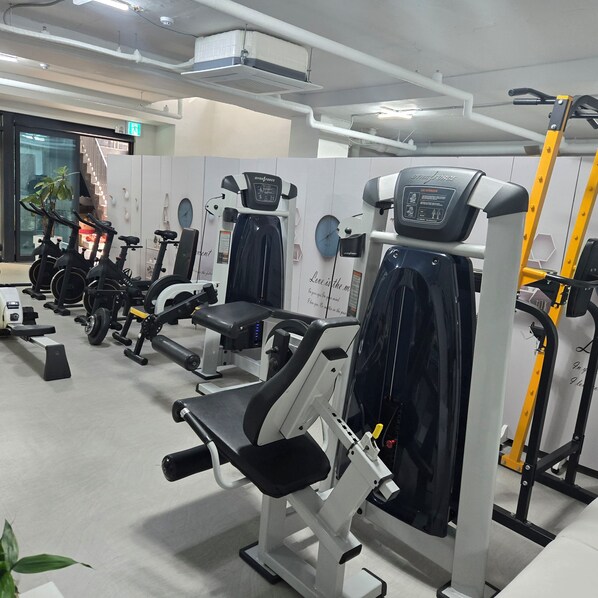 Un gimnasio con diferentes máquinas de ejercicio, un reloj y una planta.