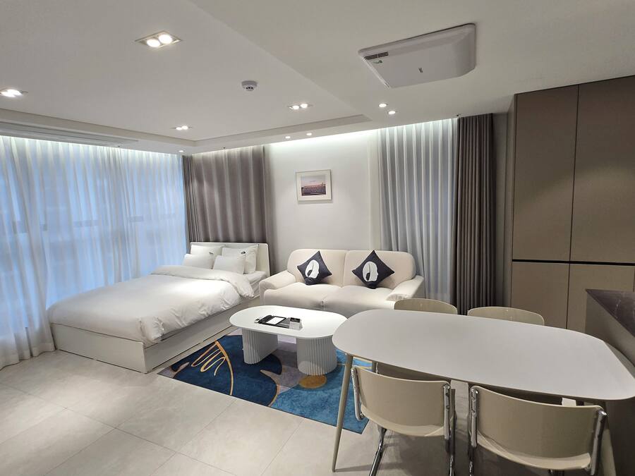 Ein modernes Hotelzimmer mit einem Bett, zwei Sofas, einem Couchtisch und einem Esstisch mit Stühlen.