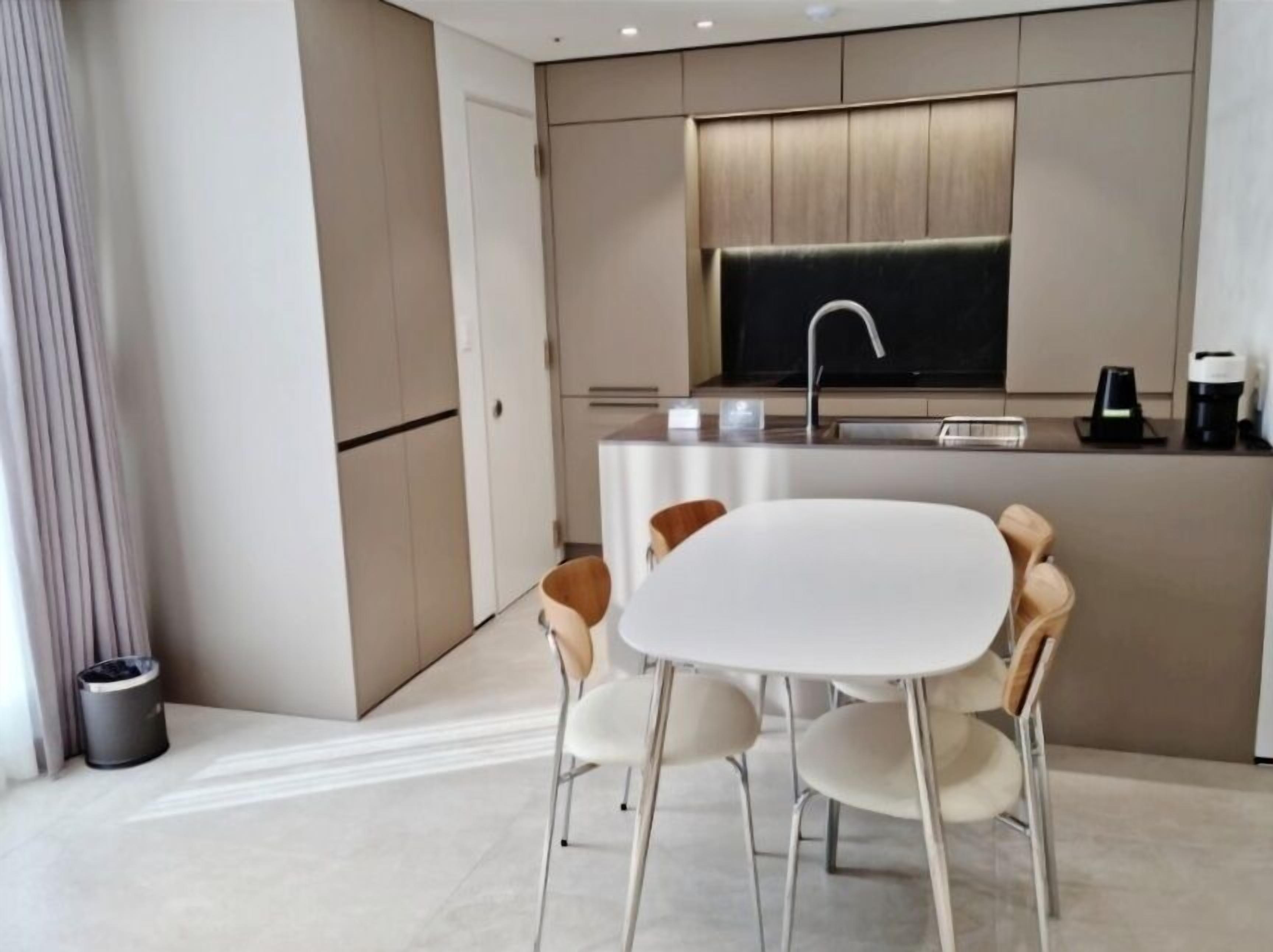 A modern kitchen with a central island, white chairs, and a coffee machine.