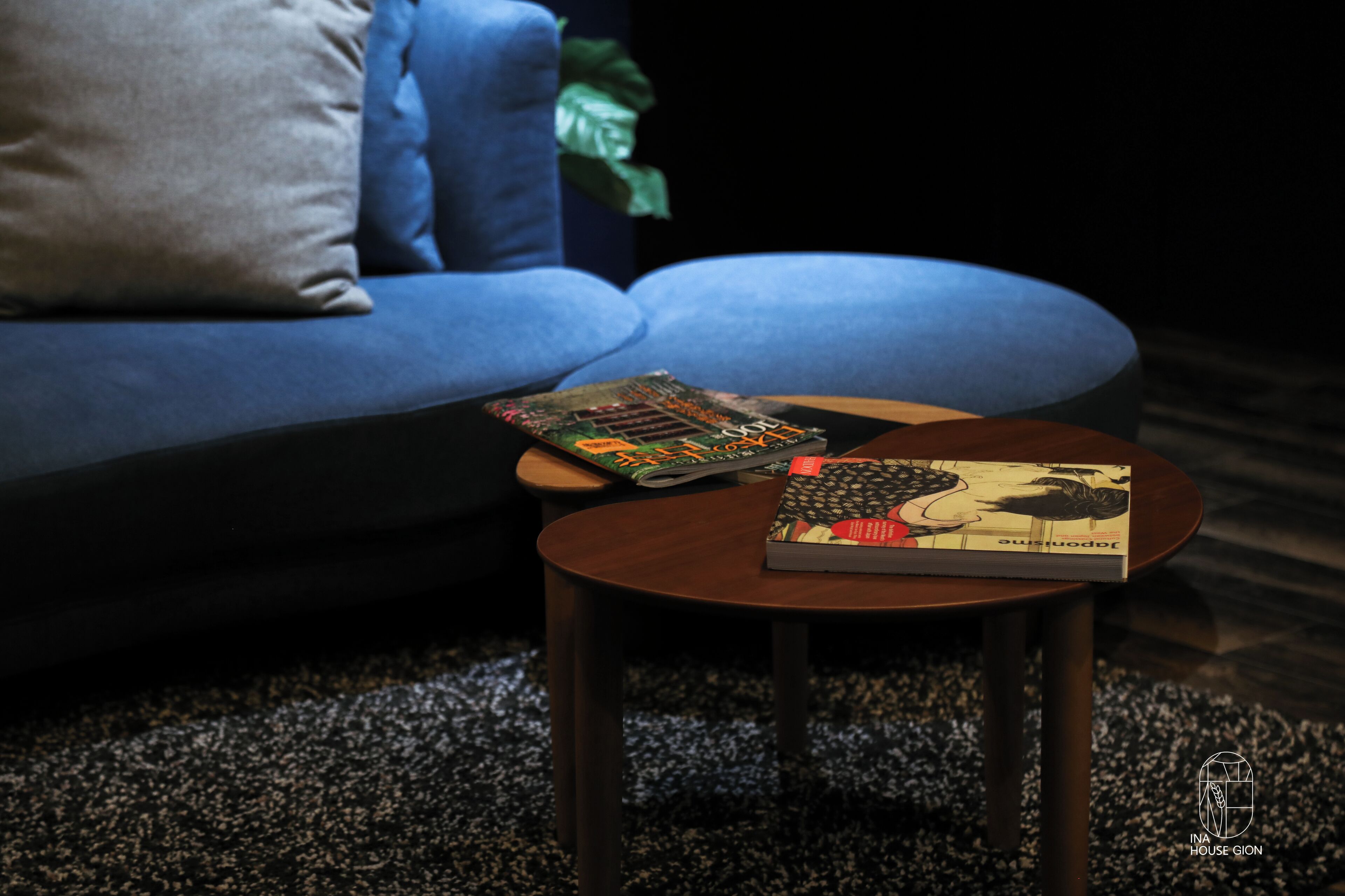 Un salon moderne avec un canapé bleu, une petite table en bois sur laquelle reposent deux livres et un tapis foncé.