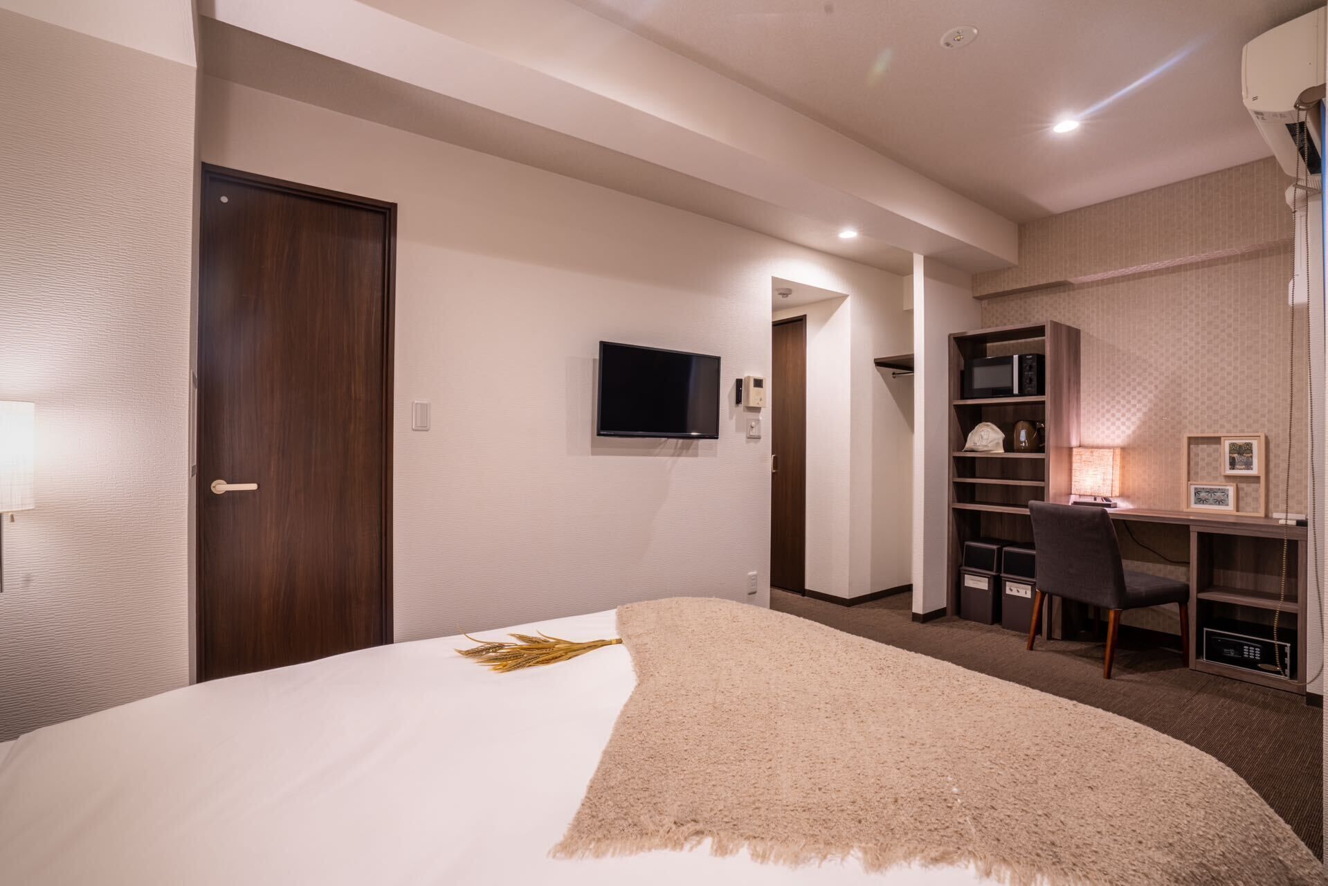 Habitación de hotel con cama, escritorio, silla, televisión y estante con objetos.