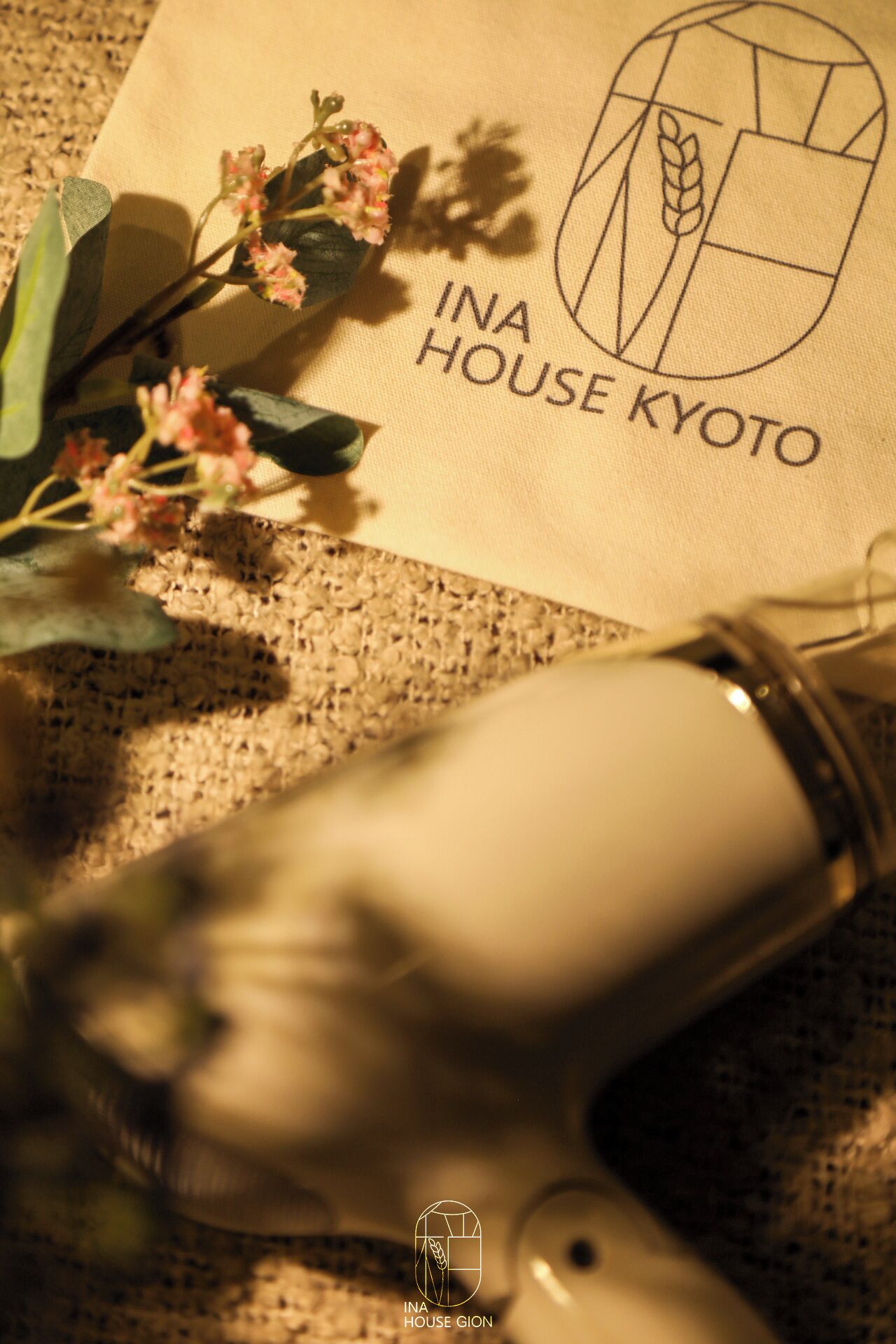 A textured fabric surface with a logo and text reading "INA HOUSE KYOTO".