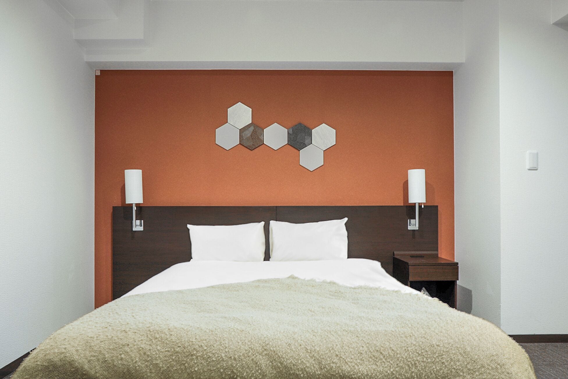 A hotel room with a large bed, two bedside lamps, a wooden headboard, and a hexagonal wall decoration.