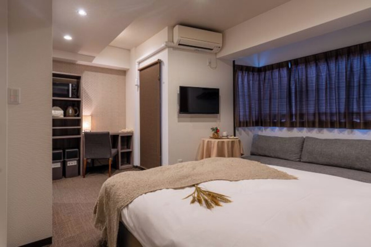 Ein Hotelzimmer mit Bett, Schreibtisch, Stuhl, Fernseher und einem Fenster mit Vorhängen.