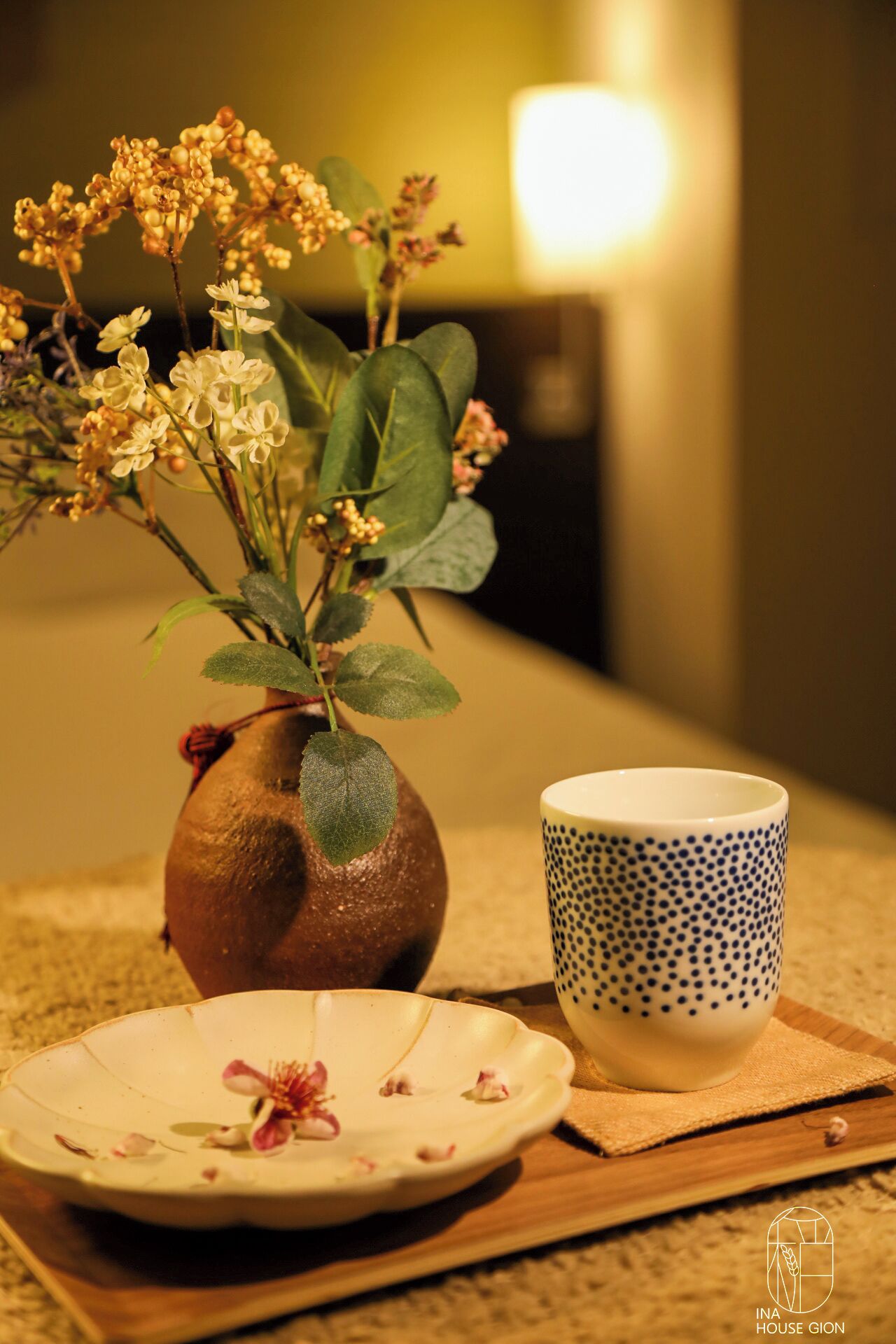 Une table sur laquelle se trouvent un vase en céramique contenant des fleurs, une tasse en céramique ornée de motifs à pois et une assiette parsemée de pétales de fleurs.