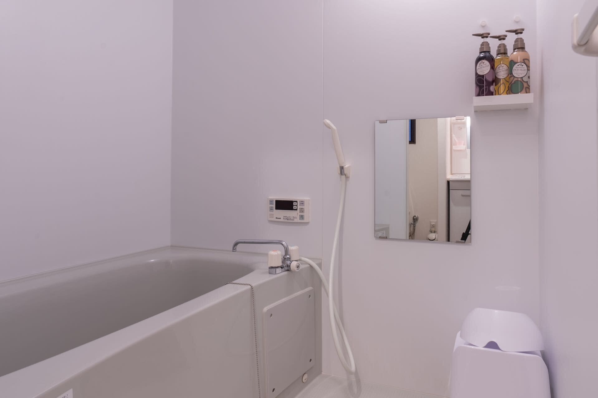A bathroom with a bathtub, a handheld showerhead, a toilet, and a shelf with toiletries.