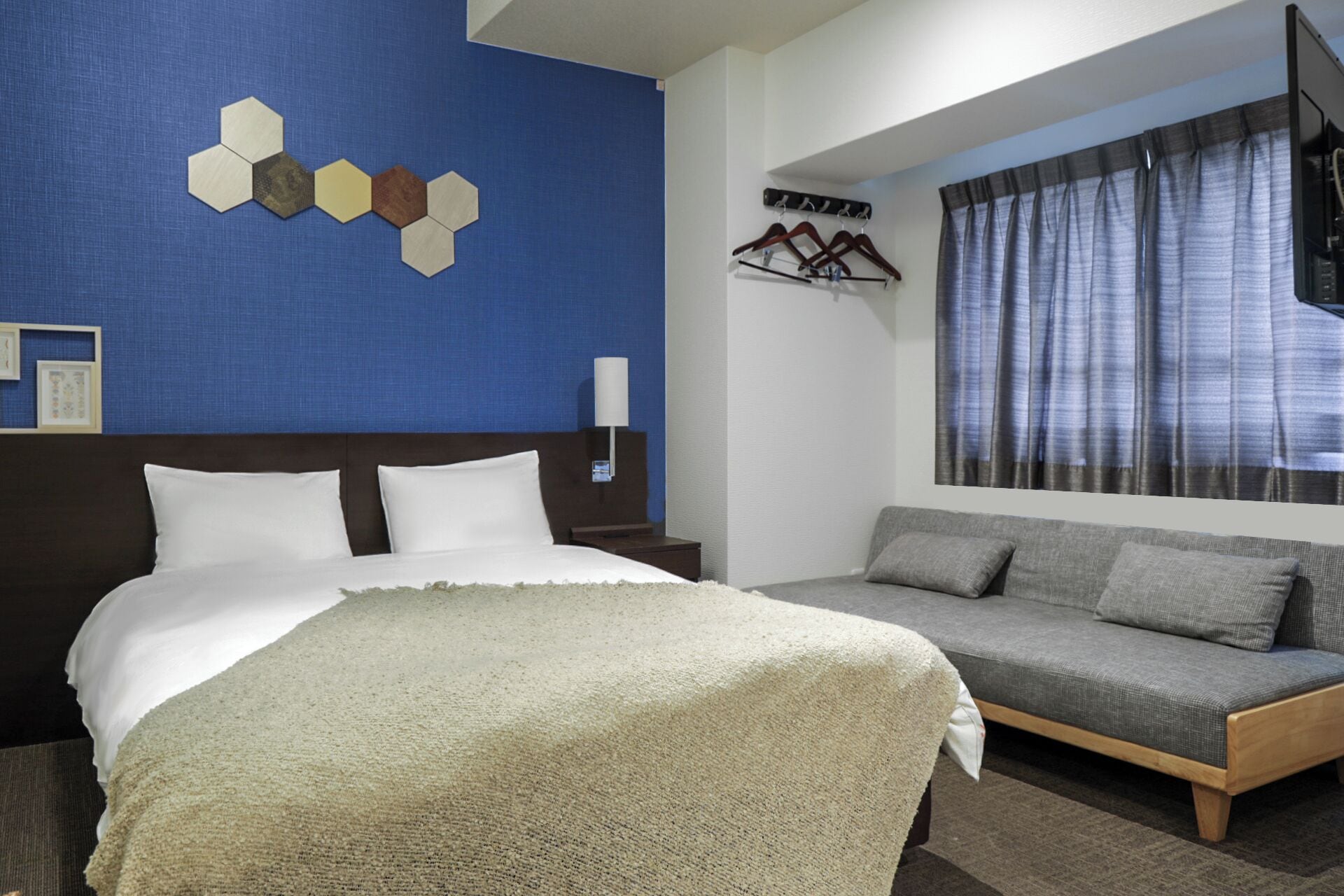 Une chambre d’hôtel avec un lit, un canapé, un téléviseur fixé au mur et une fenêtre avec des rideaux.