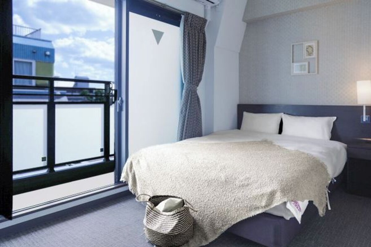 Ein Hotelzimmer mit Bett, Fenster mit Blick, Wand mit einem Bild und einem Korb mit Handtuch.