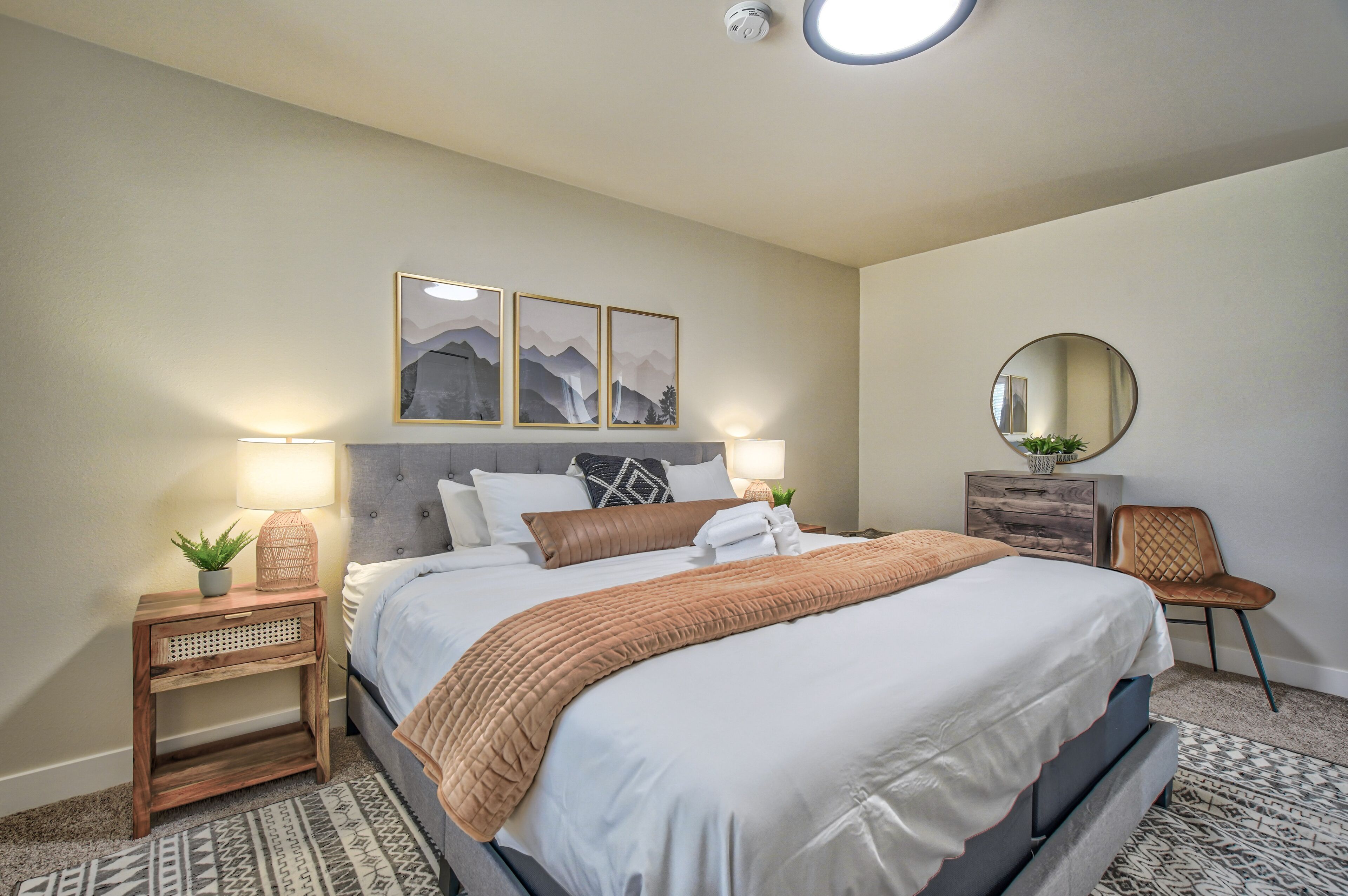 Een keurig opgemaakte slaapkamer met een bed, nachtkastjes, een spiegel en wanddecoratie.