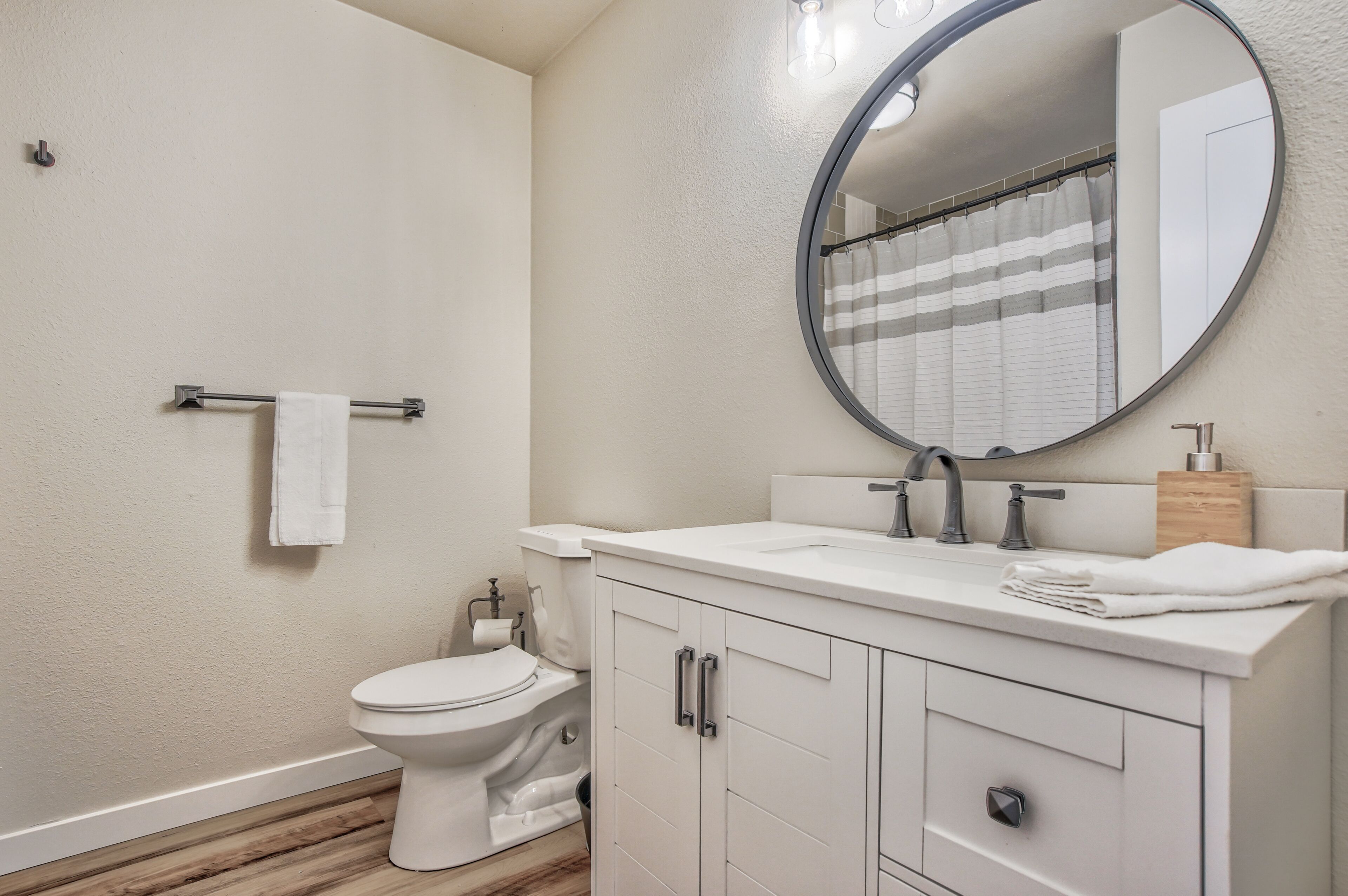 A bathroom with a toilet, sink, mirror, and towel rack.