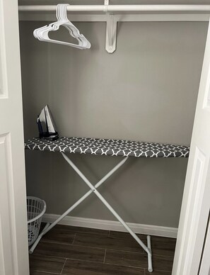 Convenient laundry area with ironing board, hanging rack, and laundry basket.
