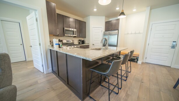 Una cocina moderna con armarios oscuros, electrodomésticos de acero inoxidable, una isla grande con taburetes y piso de madera.