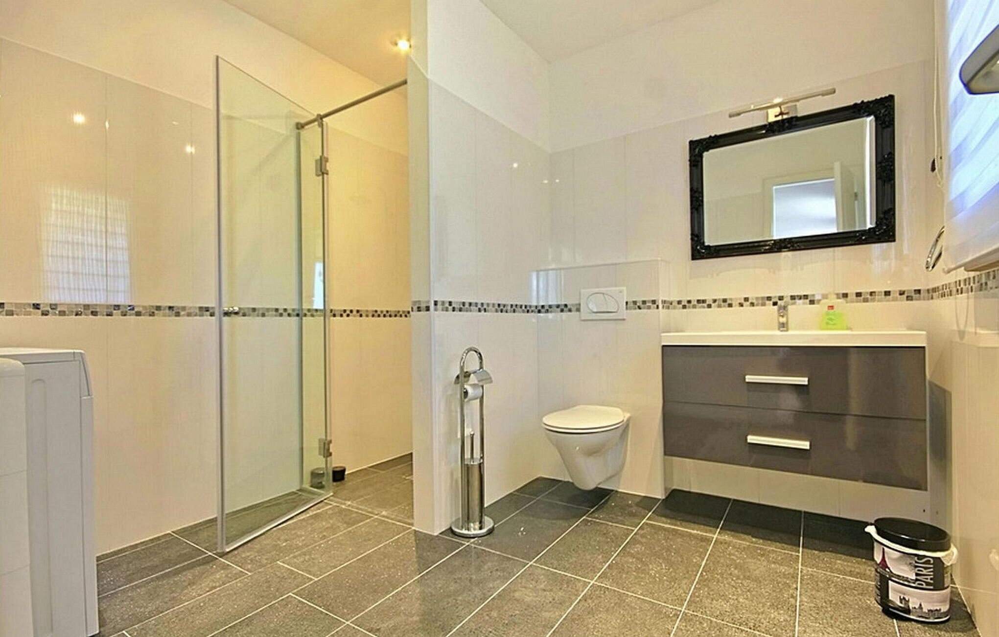 A modern bathroom with a glass shower enclosure, a toilet, a sink with a mirror, and a tiled floor.