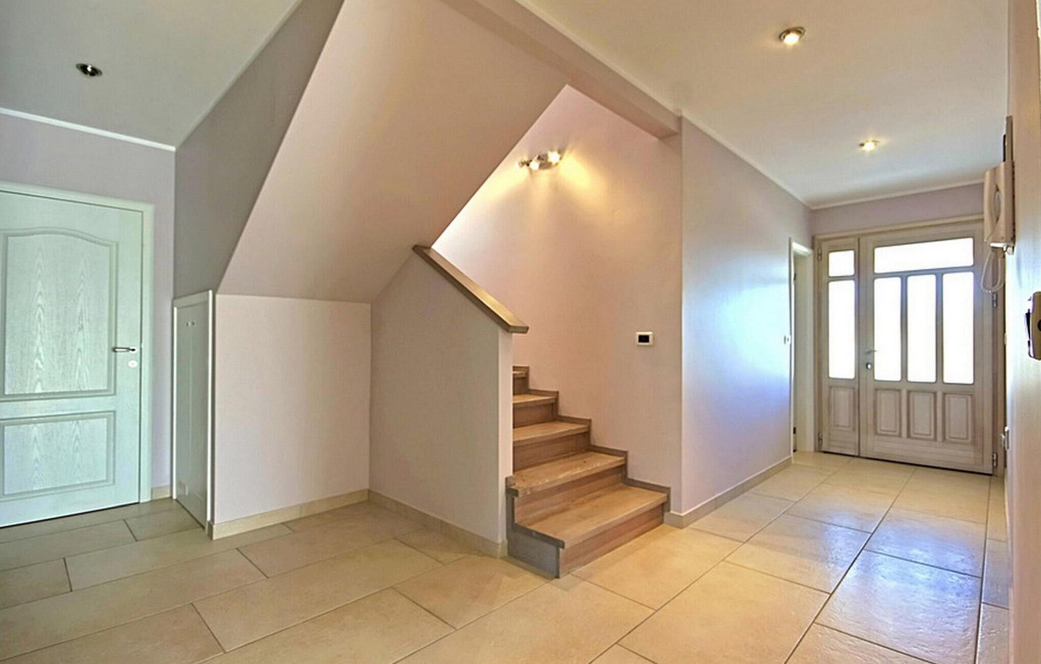 A spacious interior with a wooden staircase, light-colored walls, and a tiled floor.