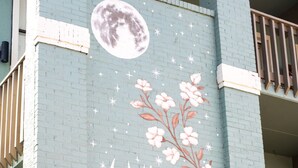 Un edificio con un mural de flores rosas y una luna sobre un muro azul verdoso.