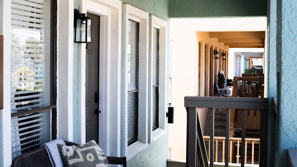 A porch with a chair and a cushion, a door, and a view into a room with a table and chairs. - 202, Ocean Side, Patio, Laundry, Desk (South Padre Island)