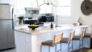A modern kitchen with a stainless steel refrigerator, a black microwave, a gas stove, and a large island with bar stools. - 202, Ocean Side, Patio, Laundry, Desk (South Padre Island)