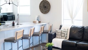 A modern kitchen with a bar area, bar stools, a black leather sofa, and a decorative wall piece. - 202, Ocean Side, Patio, Laundry, Desk (South Padre Island)