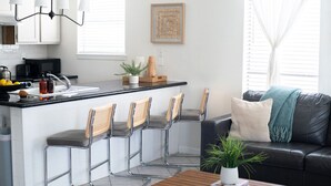 A modern kitchen with a central island, bar stools, a black leather sofa, and a coffee table with a plant. - 302, Ocean Side, Patio, Laundry, Desk (South Padre Island)