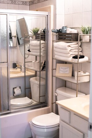 A bathroom with a glass-enclosed shower, a toilet, a sink, and shelves with towels and toiletries. - 302, Ocean Side, Patio, Laundry, Desk (South Padre Island)