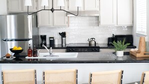 A modern kitchen with white cabinets, a stainless steel refrigerator, a black countertop, and a central island with a sink and bar stools. - 302, Ocean Side, Patio, Laundry, Desk (South Padre Island)