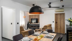 Un comedor moderno con una mesa grande dispuesta para seis personas, un ventilador de techo y un televisor montado en una pared de madera.