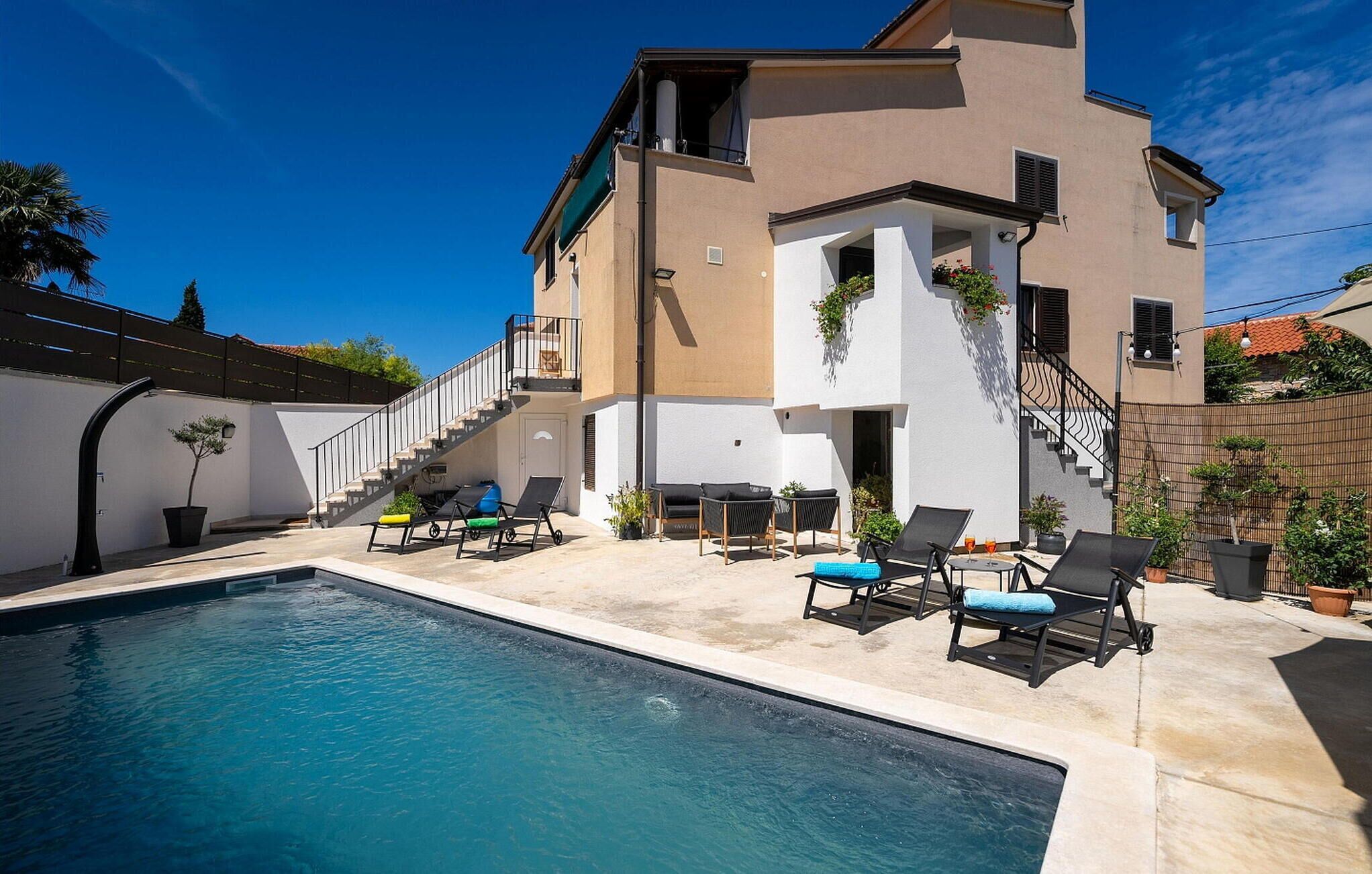 A modern building with a swimming pool, outdoor seating, and a staircase leading to an upper level.