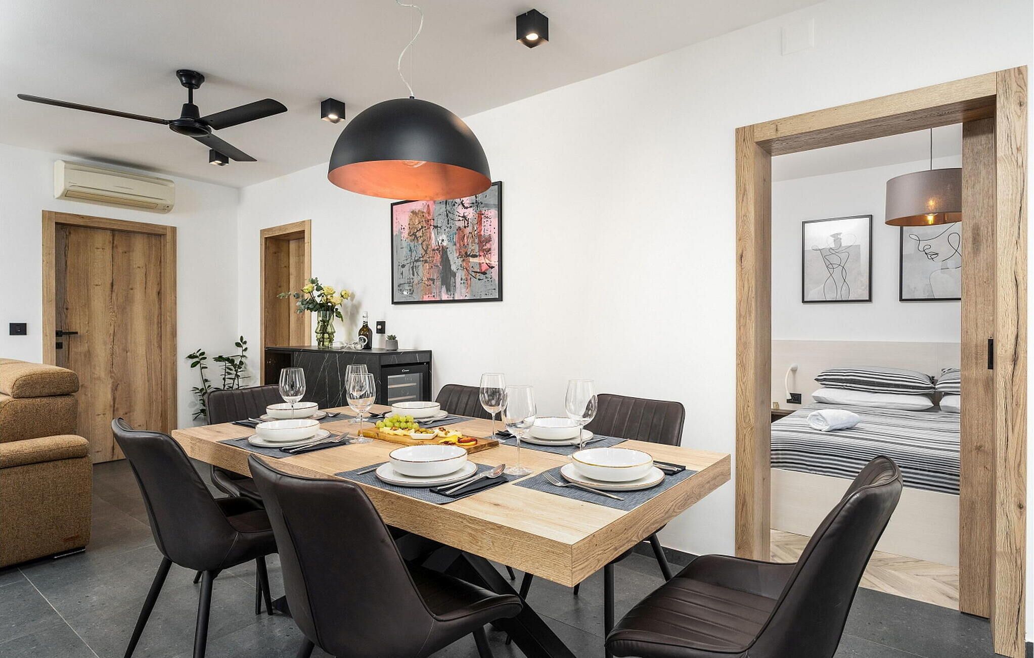 Un espace repas moderne avec une table en bois pouvant accueillir six personnes, des chaises noires et un luminaire suspendu noir.