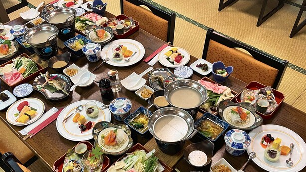 Una mesa de comedor con diversos platos y ollas calientes, rodeada de sillas.