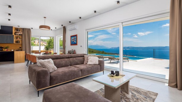 A modern living room with a large glass door leading to a balcony with a sea view.