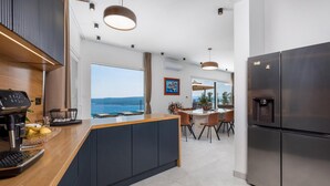A modern kitchen with a central island, a built-in refrigerator, and a view of the sea.