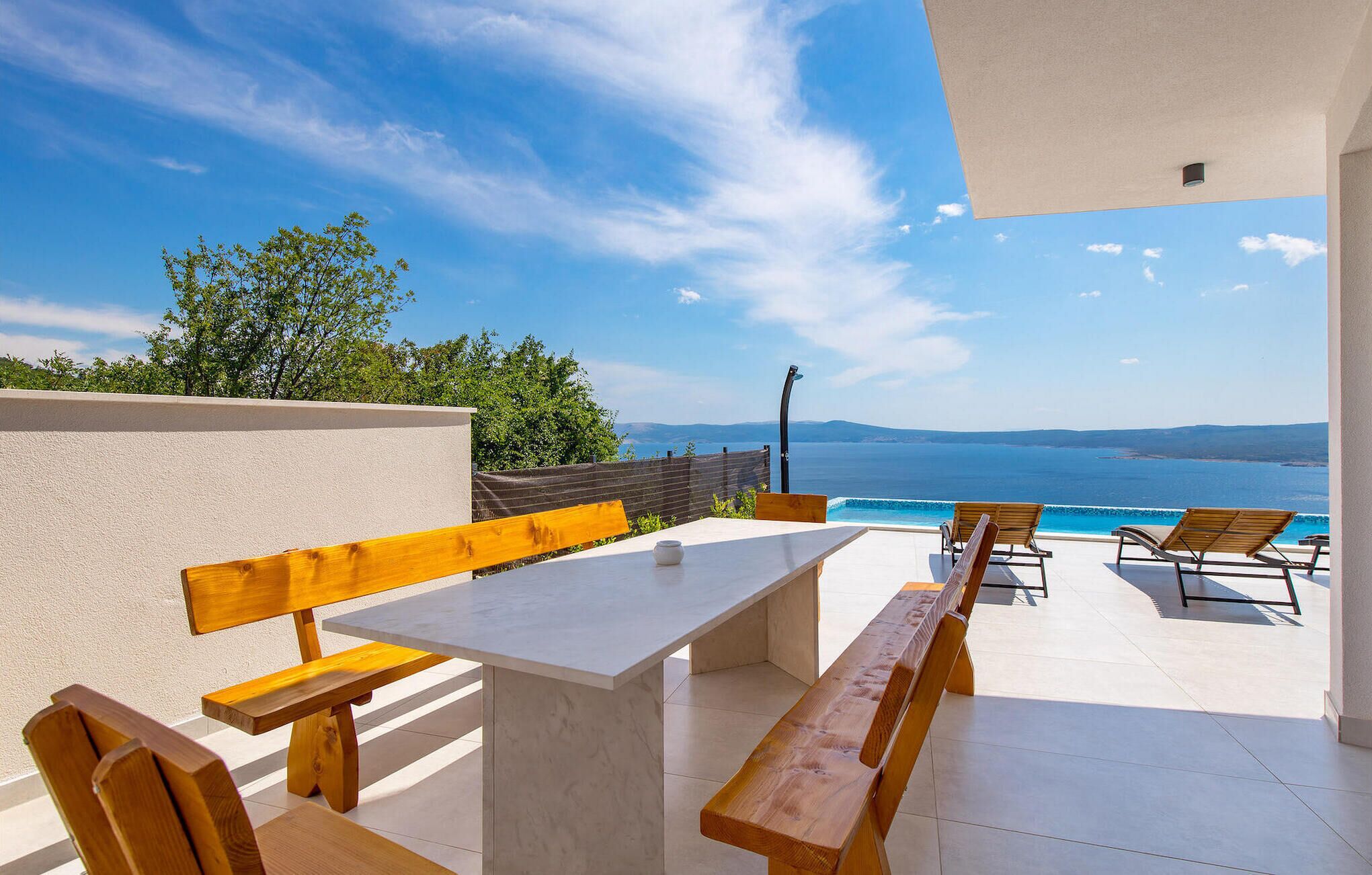 An outdoor patio with a table and benches, overlooking a body of water and distant landscape.