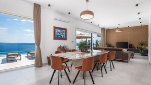 A modern living room with a glass dining table, leather chairs, a sofa, and a TV.