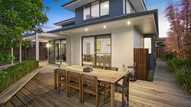 A modern house with a wooden deck, a dining area with a table and chairs, and a garden with a wooden fence.