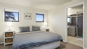 A bedroom with a bed, two bedside tables, a nightstand, a window, and a door leading to a bathroom.