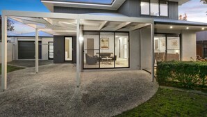 A modern two-story house with a covered patio area, large windows, and a well-maintained lawn.
