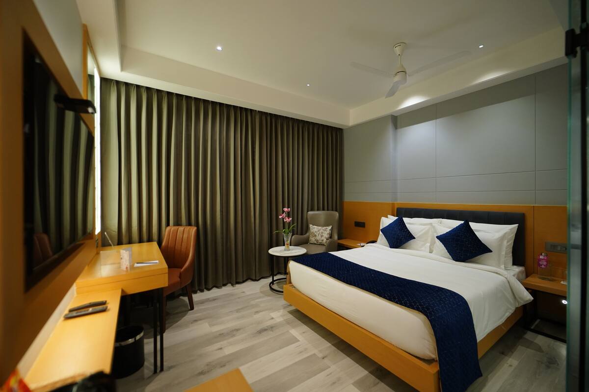 A modern hotel room with a large bed, a desk, a chair, and a small table with a vase of flowers.