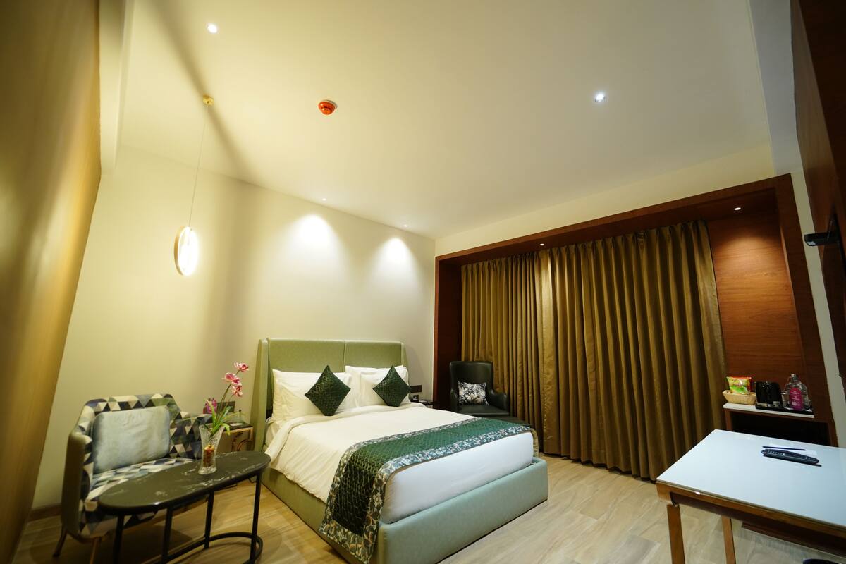 A hotel room with a bed, a desk, a chair, a table, and a curtain.