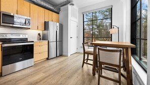 A modern kitchen with stainless steel appliances, wooden cabinets, and a large window offering a view of trees.