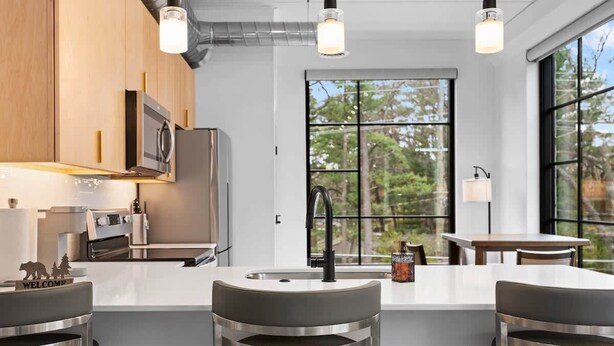 A modern kitchen with a central island, stainless steel appliances, and a large window offering a view of trees.
