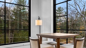 A dining area with a table and chairs, large windows, and a wall-mounted lamp.
