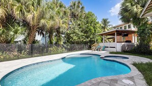 A swimming pool with a curved design, surrounded by a stone patio and lush greenery.