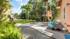 A residential area with a playground, including a slide and swings, surrounded by lush greenery and palm trees.