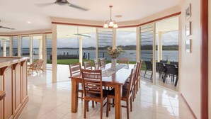 A dining area with a large table and chairs, a ceiling fan, and a view of a body of water through large windows.