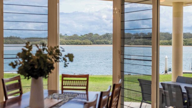 A dining area with a view of a lake, a table with chairs, and a vase with flowers.