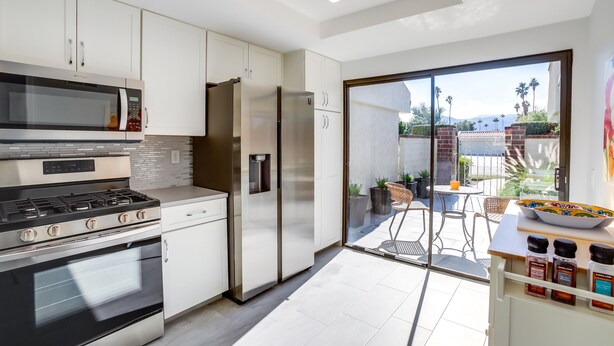 Una cucina moderna con elettrodomestici in acciaio inossidabile, mobili bianchi e una porta scorrevole in vetro che dà su un patio esterno.