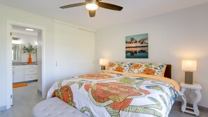 Una camera da letto con un letto grande, una ventola a soffitto, un comodino con una lampada e un quadro appeso al muro.