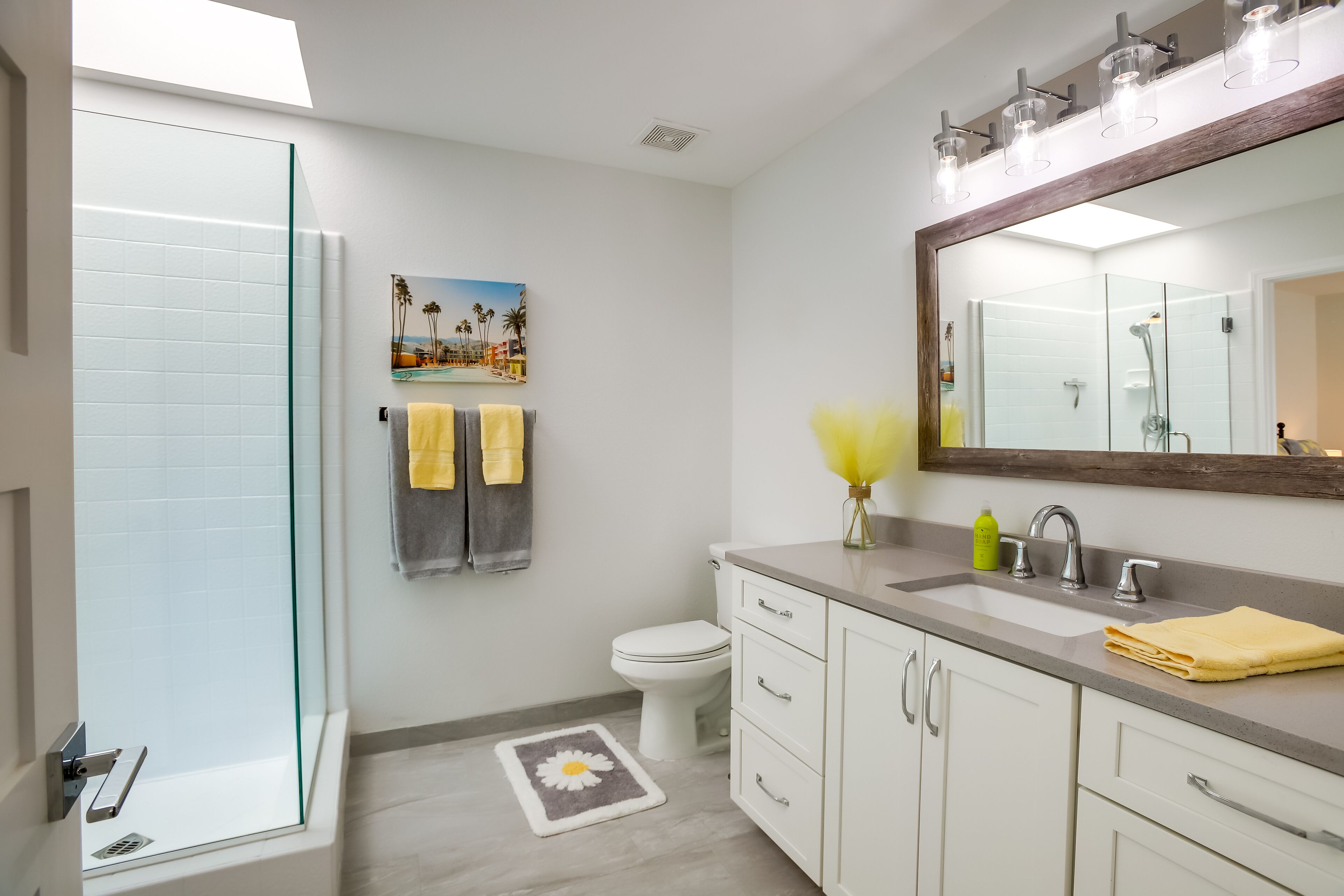 A bathroom with a glass shower enclosure, a toilet, a sink with a mirror, and a towel rack with yellow towels.