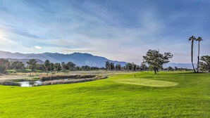 Un campo da golf con uno stagno, palme e montagne sullo sfondo.